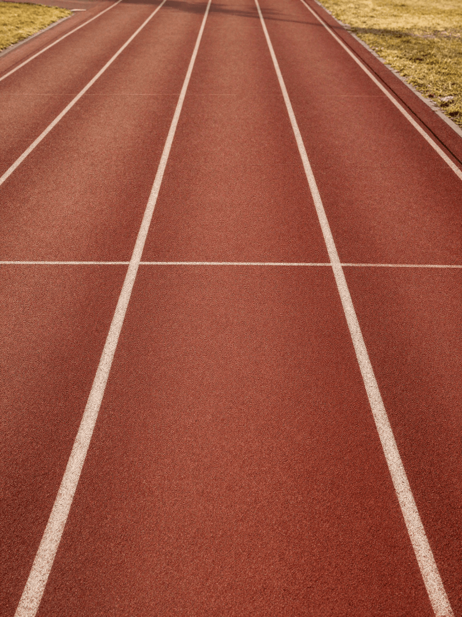 Empty athletics running track at dawn, lane markings in soft warm light - the quiet structure that holds a career.