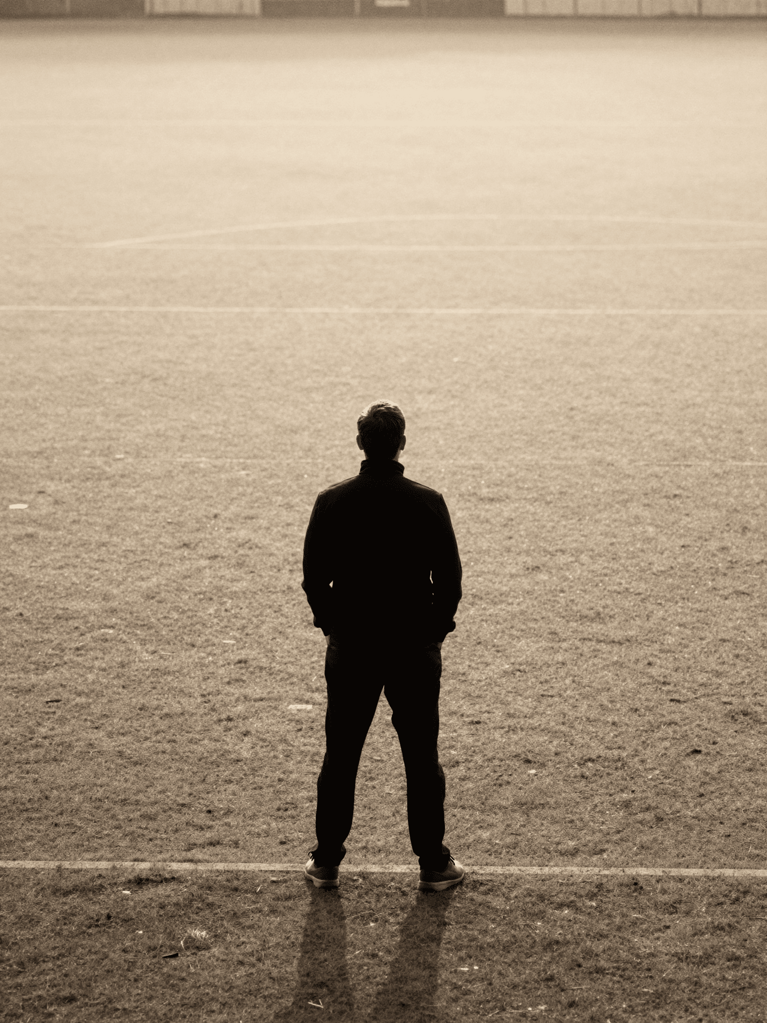 A lone figure standing still at the edge of an empty field at dawn, quietly observing - counsel kept in confidence.
